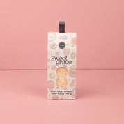 The Bridgewater Candle Sweet Grace Body Wash Sponge stands upright against a plain pink background, its patterned light packaging with a dark handle offering creamy lather for gentle skin exfoliation.