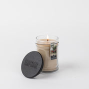 A lit Afternoon Retreat 8oz Jar Candle by Bridgewater Candle Company sits in a clear glass jar with a black lid and tag featuring the scent image, all displayed on a white background.
