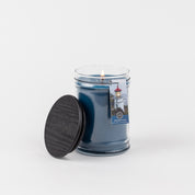 A lit Bridgewater Candle Company Nantucket Coast 18oz Large Jar Candle with a black lid sits beside it. The label shows a lighthouse, referencing the Nantucket Coast scent, all set against a plain white background.
