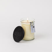 A Bridgewater Candle Company Laundry Line 18oz Large Jar Candle made from a soy-blend burns in a clear glass jar with a black wooden lid and small tag, set against a plain white background.