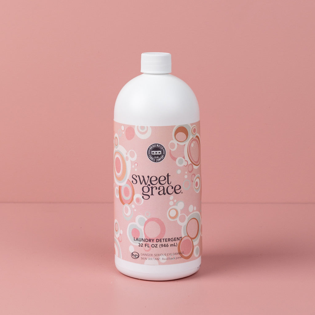 Bridgewater Candle Companys Sweet Grace 32oz Laundry Detergent features a pink label with circular patterns and comes in a white bottle with a white cap, displayed against a matching pink background.