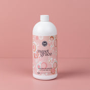 Bridgewater Candle Companys Sweet Grace 32oz Laundry Detergent features a pink label with circular patterns and comes in a white bottle with a white cap, displayed against a matching pink background.