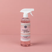 A pink spray bottle of Bridgewater Candle Company Sweet Grace Multi-Surface Cleaner with a white nozzle stands against a pink background. Its white and pink striped label highlights the signature Sweet Grace fragrance.