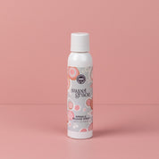 A white Bridgewater Candle Company Sweet Grace Wrinkle Release Spray bottle stands upright on a pink surface with a pink background. The label displays pink and orange circular patterns.