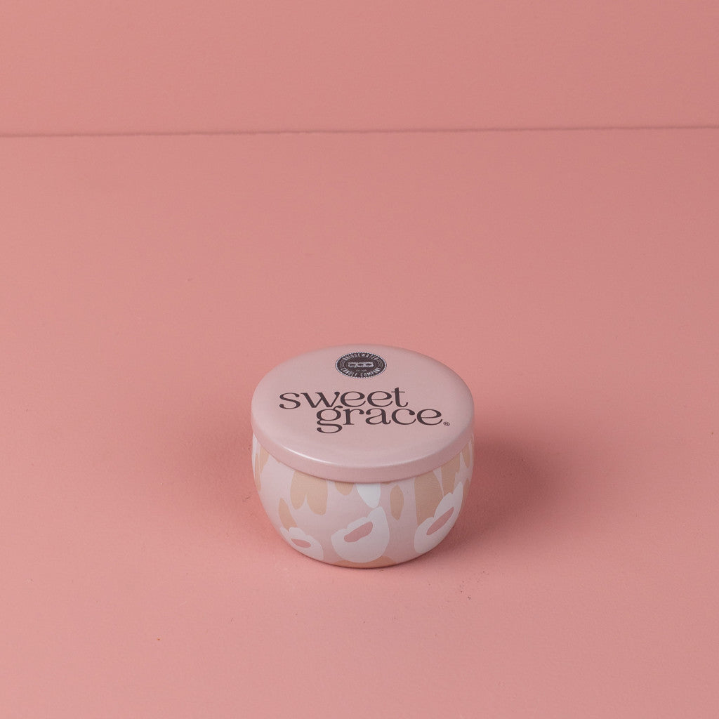 The Bridgewater Candle Company Sweet Grace Collection Candle #059 is a small, round tin with a light pink lid, featuring beige and white abstract patterns. This travel-sized candle is crafted with luxurious soy-blend wax.