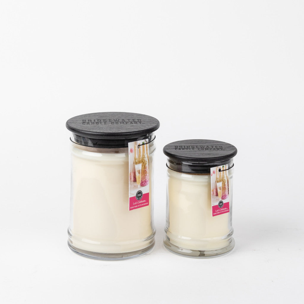 Two Bridgewater Candle Company Lets Celebrate 18oz Large Jar Candles with black lids sit side by side. Each clear glass jar features a product tag with champagne glasses and a pink accent for an elegant touch.