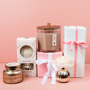 A collection of pink and white gifts, featuring the Bridgewater Candle Company Sweet Grace Mercury Flower Diffuser and candles, arranged with wrapped boxes—perfect for adding a delightful home fragrance to any space.