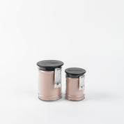 Two Sweet Grace 8oz Jar Candles by Bridgewater Candle Company—pink-beige in clear glass jars with black lids and white labels, one large and one small—sit side by side on a white background, evoking a warm, inviting aroma.