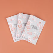 Three Bridgewater Candle Company Sweet Grace Modern Bubble Sachets, featuring pink and white bubble designs, are arranged in a fan shape on a peach background—ideal for adding a delightful fragrance to your home.