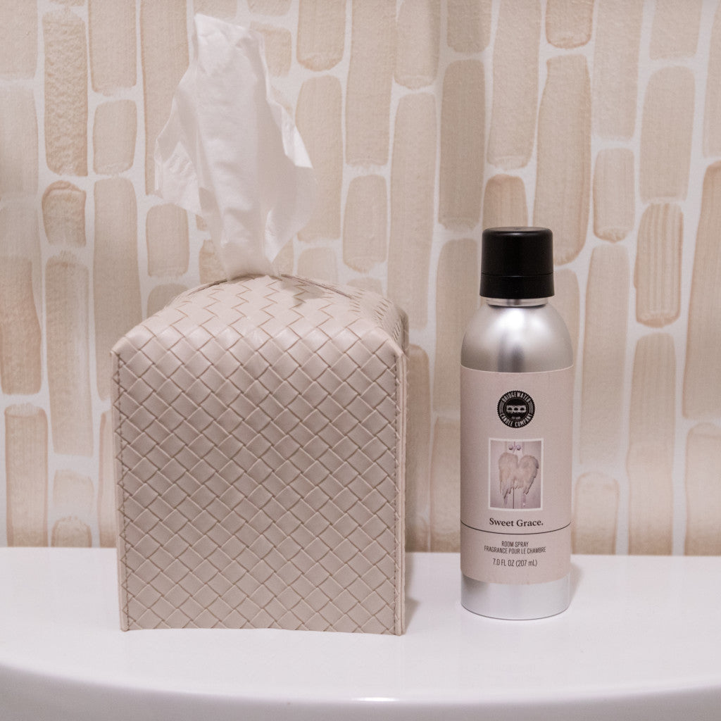 A woven-patterned tissue box sits beside a Bridgewater Candle Company Sweet Grace Non-Aerosol Room Spray on a white surface, set against a beige textured background.