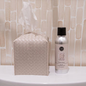 A woven-patterned tissue box sits beside a Bridgewater Candle Company Sweet Grace Non-Aerosol Room Spray on a white surface, set against a beige textured background.