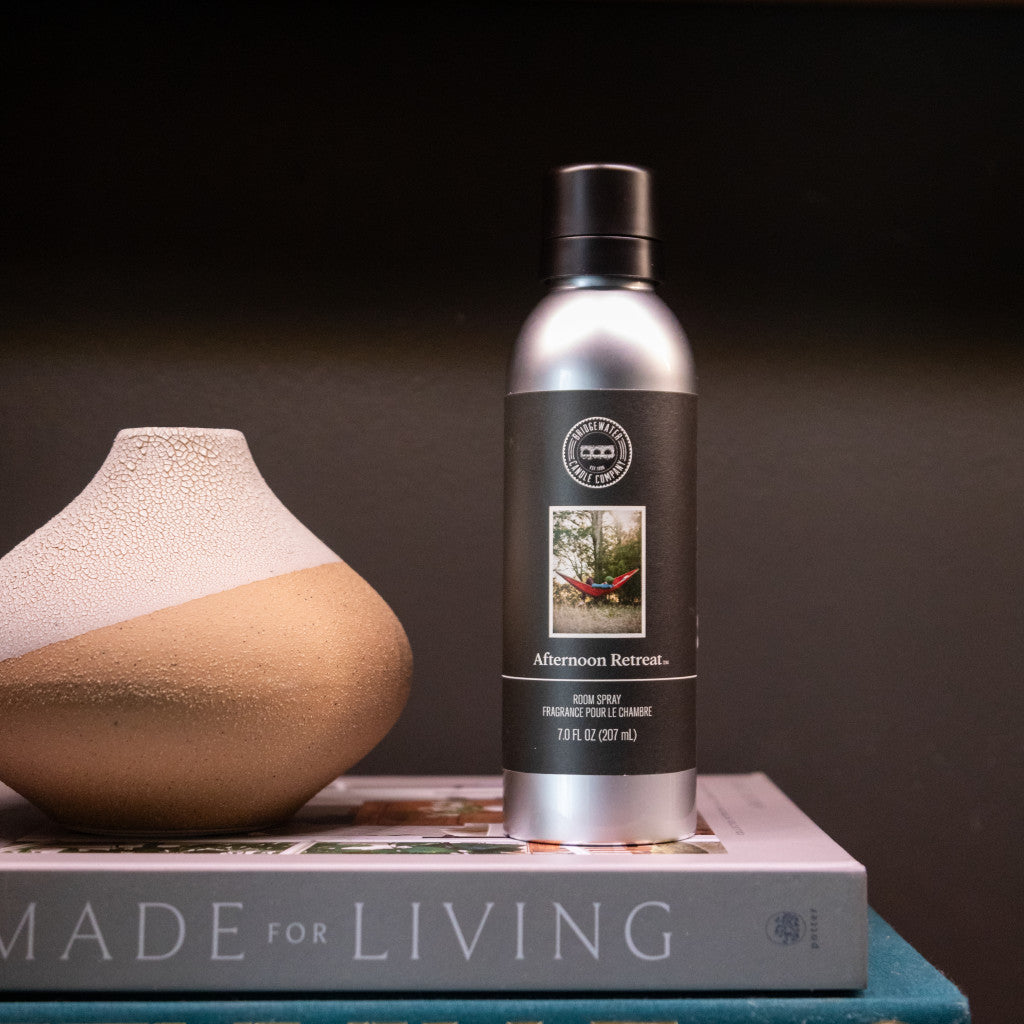 A silver bottle of Bridgewater Candle Companys Afternoon Retreat Non-Aerosol Room Spray sits beside a textured vase on Made for Living, adding a premium home fragrance accent to the dark background.