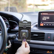 A hand holds a Bridgewater Candle Company Afternoon Retreat Auto Vent Clip in a car, with the dashboard showing Taylor Swifts Blank Space on the music screen, plus the steering wheel and air vent in view.