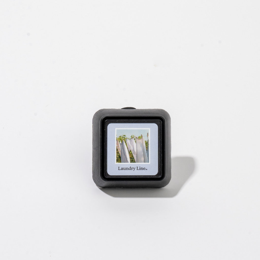 The Bridgewater Candle Company’s Laundry Line Auto Vent Clip is a small, square black car air freshener featuring laundry on a clothesline. Perfect for your car, it fills your ride with the scent of fresh laundry.