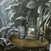 Three Bridgewater Candle Company Afternoon Retreat Flameless Bundle wax melts are displayed on a round table against leafy monochrome wallpaper, with the center package showing a red hammock in the woods.