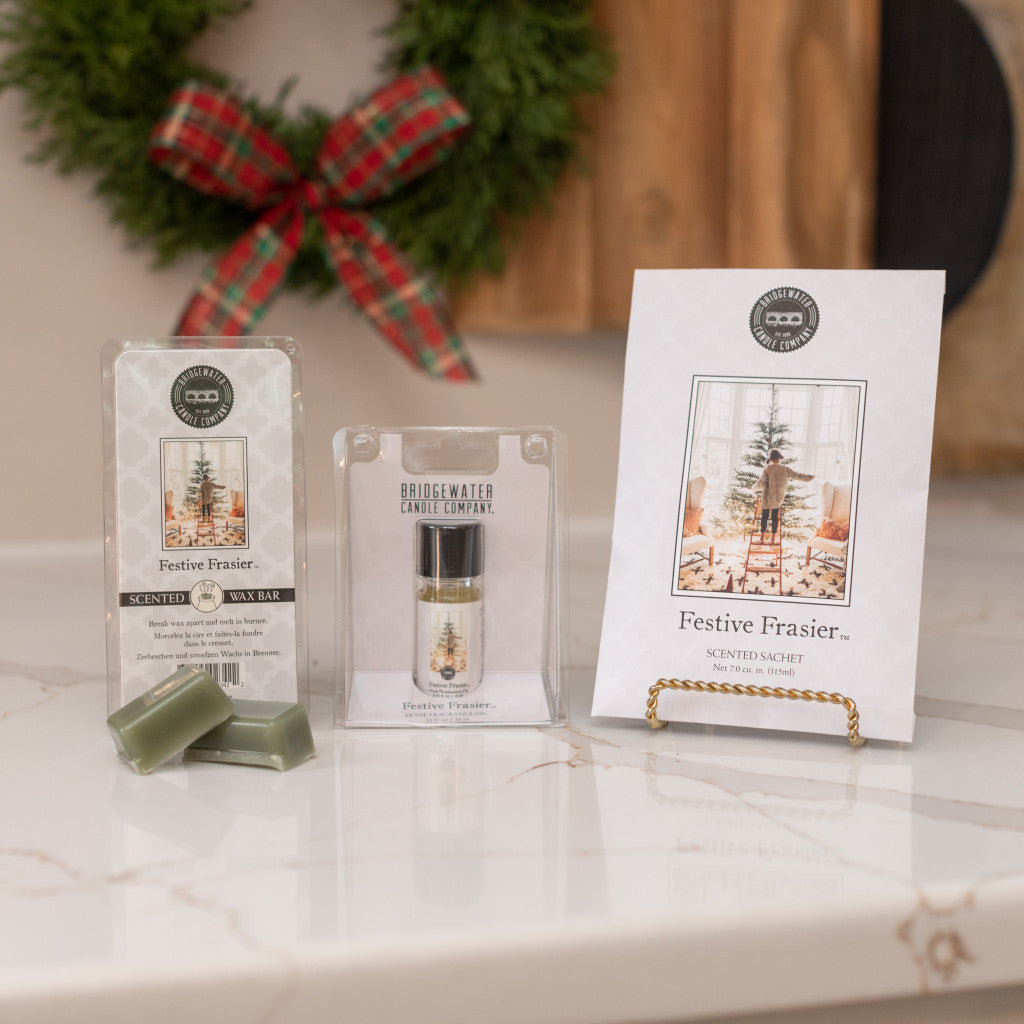 A Festive Frasier Flameless Bundle from Bridgewater Candle Company—featuring a soy-blend wax bar, small candle, and sachet—is beautifully displayed on a marble countertop with a holiday wreath. Ideal for gifting this season.