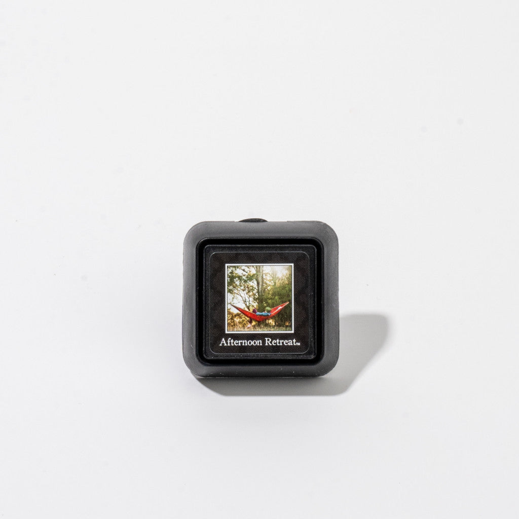 The Afternoon Retreat Auto Vent Clip by Bridgewater Candle Company is a small black square with a red hammock label, designed to bring the signature fragrance to your car.