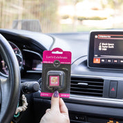 A person holds a Bridgewater Candle Company Lets Celebrate Auto Vent Clip in a car. The dashboard display shows Blank Space by Taylor Swift playing, with vent clips and dashboard controls visible.