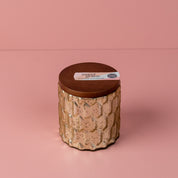 A textured ceramic jar with a wooden lid sits on a pink surface. The lid label reads Sweet Grace Collection Candle #035 by Bridgewater Candle Company, featuring their best-selling fragrance in a soy-blend wax candle.