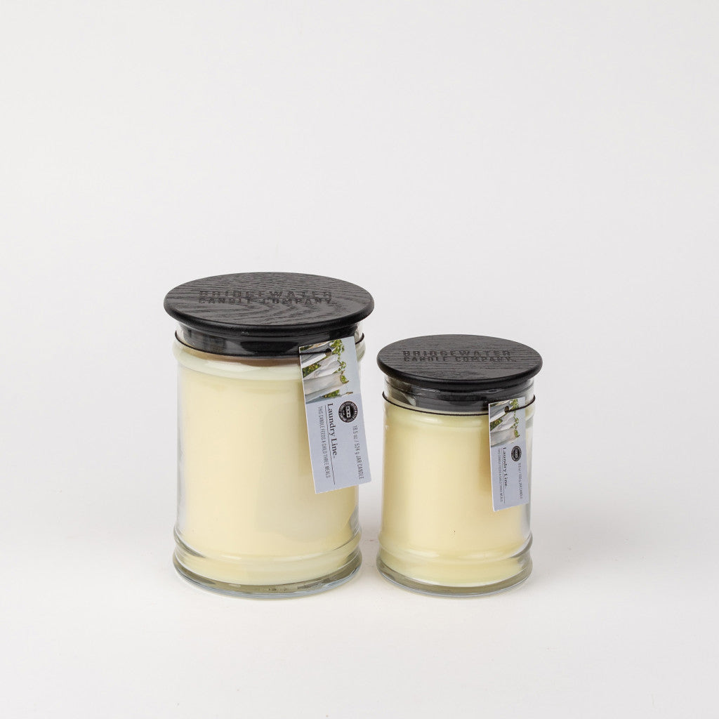 Bridgewater Candle Companys Laundry Line 18oz Large Jar Candle, featuring creamy white soy-blend wax in a glass jar with a black lid and product tag, is displayed alongside another jar against a plain white background.