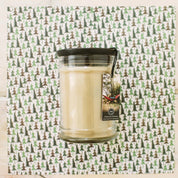 A cream-colored Bridgewater Candle Company Afternoon Retreat 8oz Jar Candle with a black lid sits on pine-patterned paper. Its label shows a hammock between trees, capturing the calm of an afternoon escape.