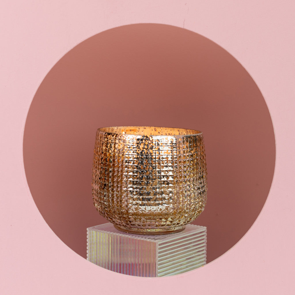 A textured, gold-colored round vase rests on a translucent pedestal against a pink backdrop, echoing the elegance of Bridgewater Candle Companys Sweet Grace Collection Candle #051—our signature best-seller.