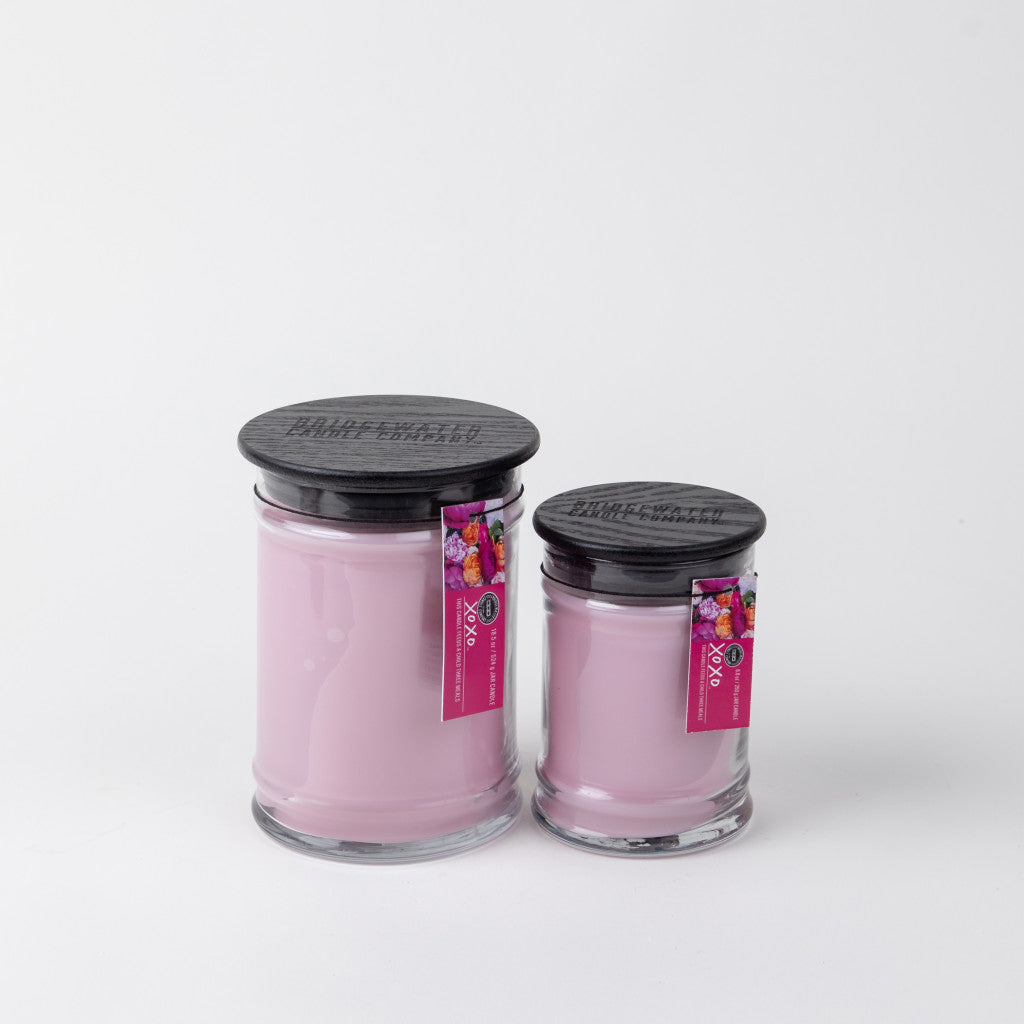 Two XOXO 8oz Small Jar Candles by Bridgewater Candle Company with black lids and light pink soy-blend wax sit side by side on a white background. Each jar has a pink floral label attached to the lid.