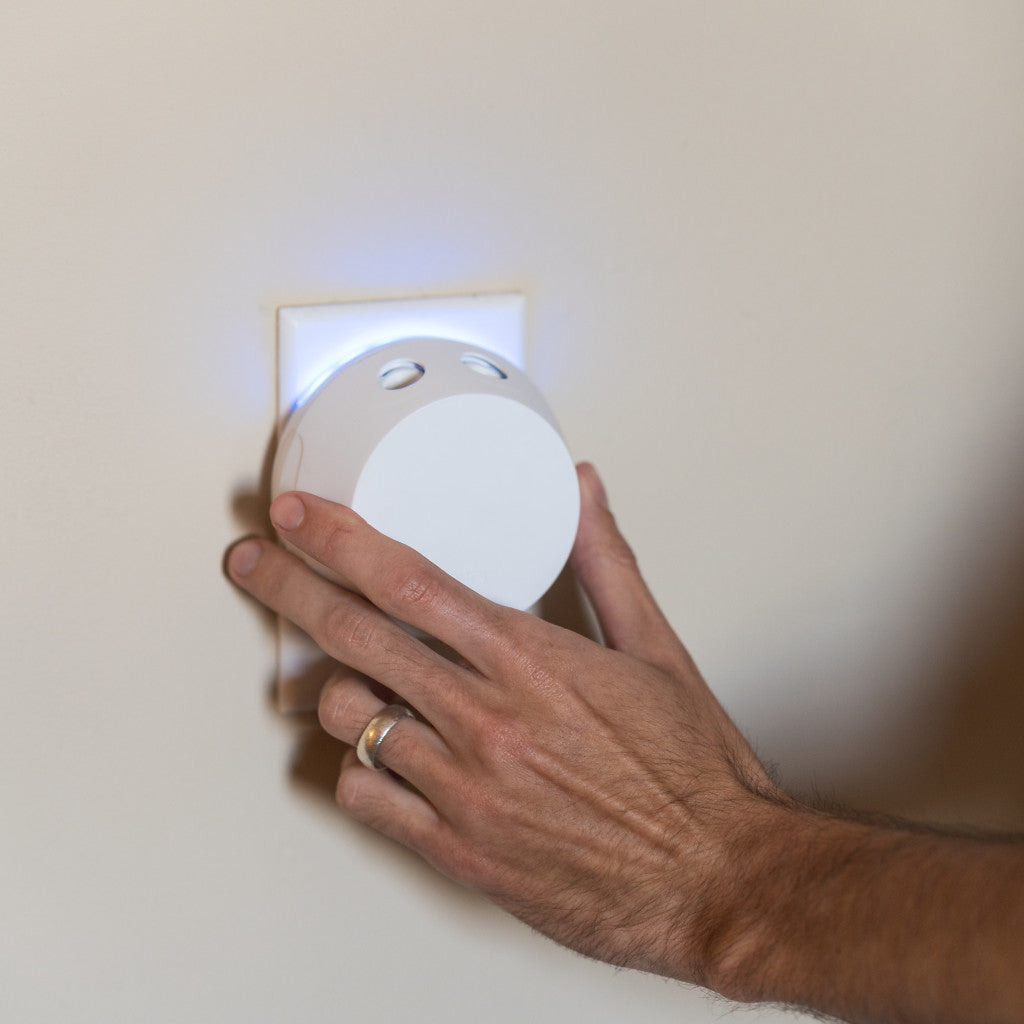 A hand with a gold ring presses the Pura + Bridgewater Sweet Grace Lovers Kit by Bridgewater Candle Company, glowing blue, into a wall outlet—ready to fill the room with Sweet Grace fragrance from this sleek smart diffuser.