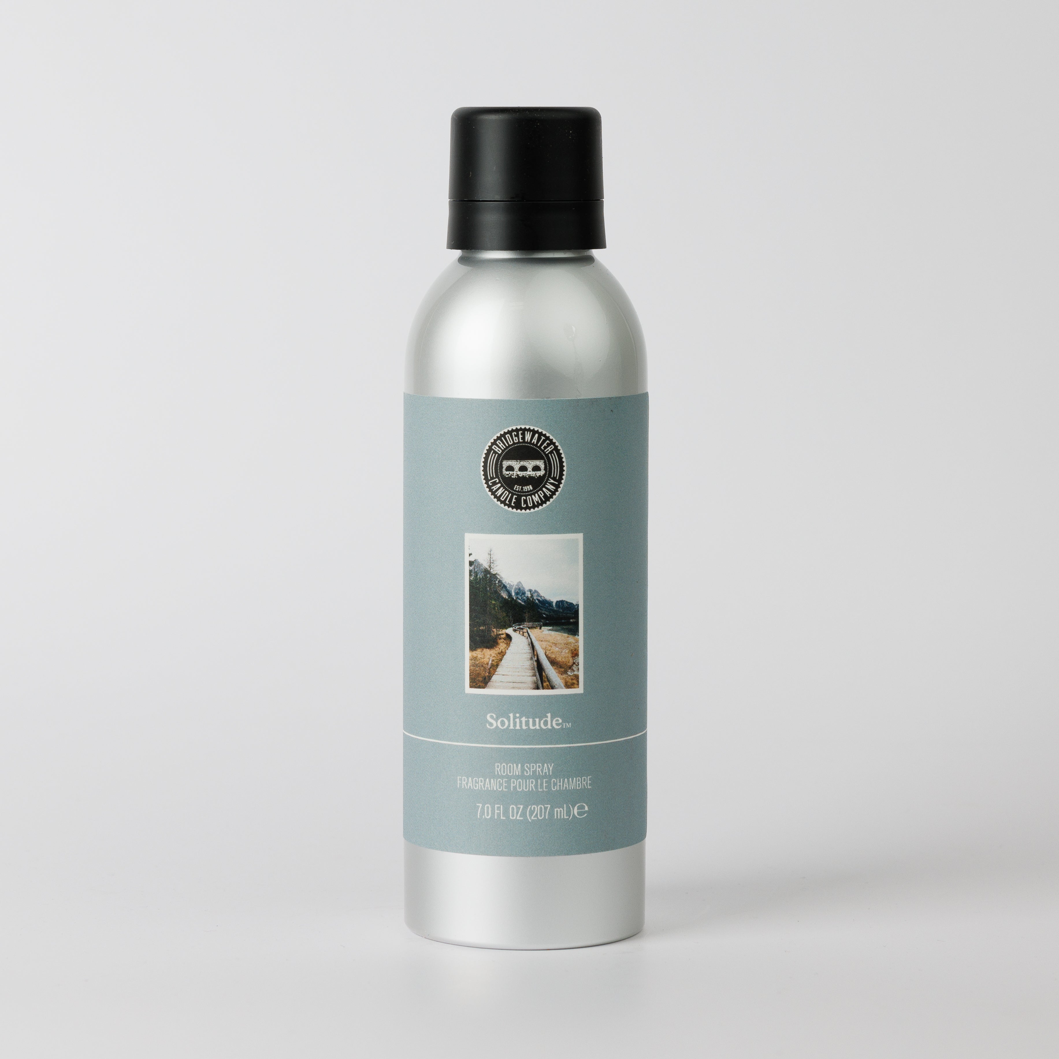 A silver bottle of Bridgewater Candle's Solitude Non-Aerosol Room Spray (7 oz/207 mL) features a blue label with a small landscape photo, black cap, and sits against a plain white background. Perfect for home fragrance.