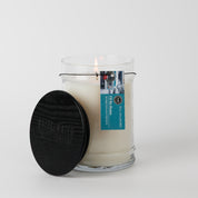 The Bridgewater Candle "I'll Be Home" 18oz Large Jar Candle, made with soy-blend wax, sits in a clear glass jar with a black wooden lid and blue label, filling your room with fragrance against a plain white background.