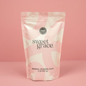 A 2 lb (907 g) pink and white resealable bag of Bridgewater Candle’s Sweet Grace Soaking Salts with Pink Himalayan sea salt stands upright against a solid pink background.