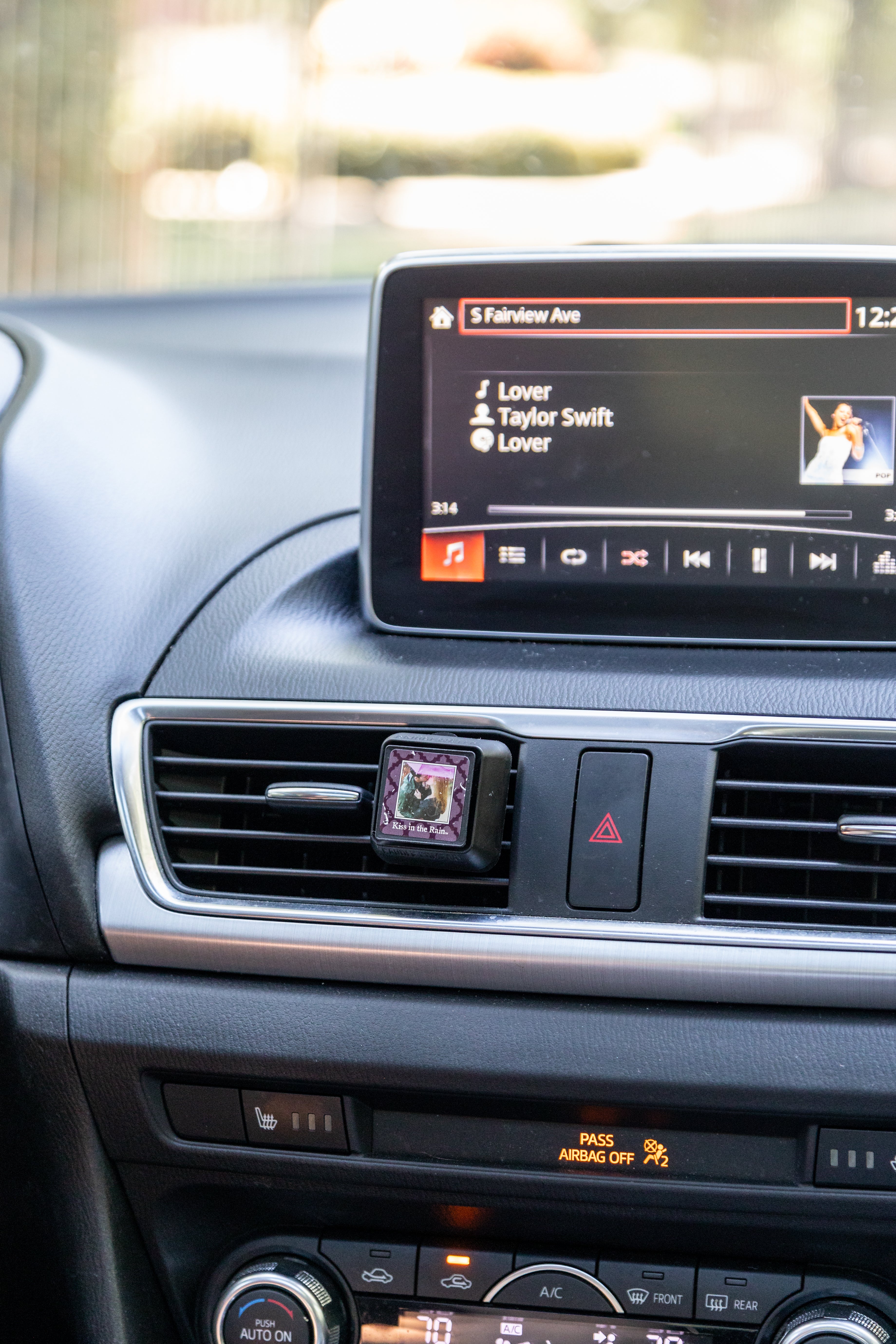 A square Auto Vent Clip-Kiss in the Rain fragrance air freshener clipped to a car’s dashboard vent.