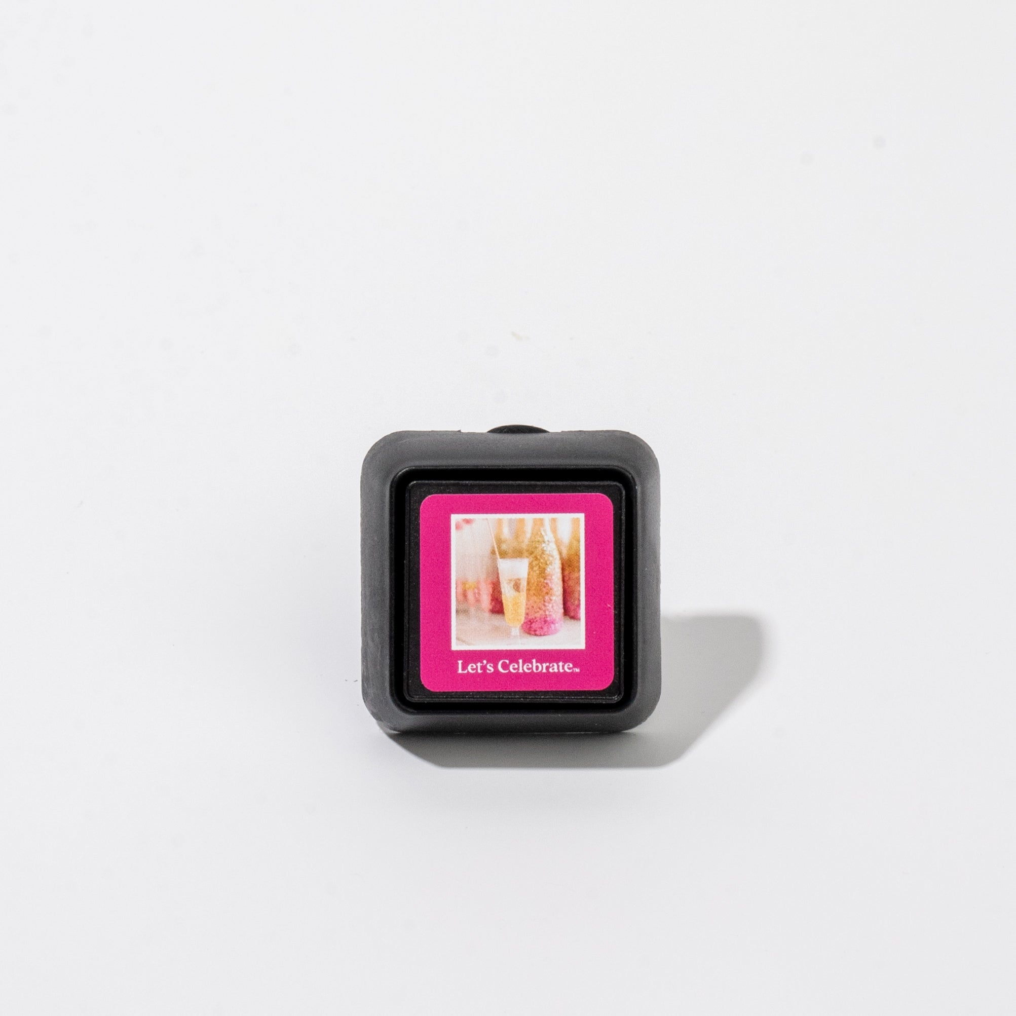 Bridgewater Candle Auto Vent Clip-Let’s Celebrate square car air freshener featuring a pink frame around an image of a champagne glass and the text Lets Celebrate.