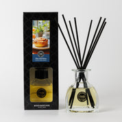 The Bridgewater Candle Rise & Shine Reed Diffuser features a clear bottle with yellow liquid and black reeds, in packaging with cinnamon rolls, to fill your home with the comforting scent of cinnamon rolls.