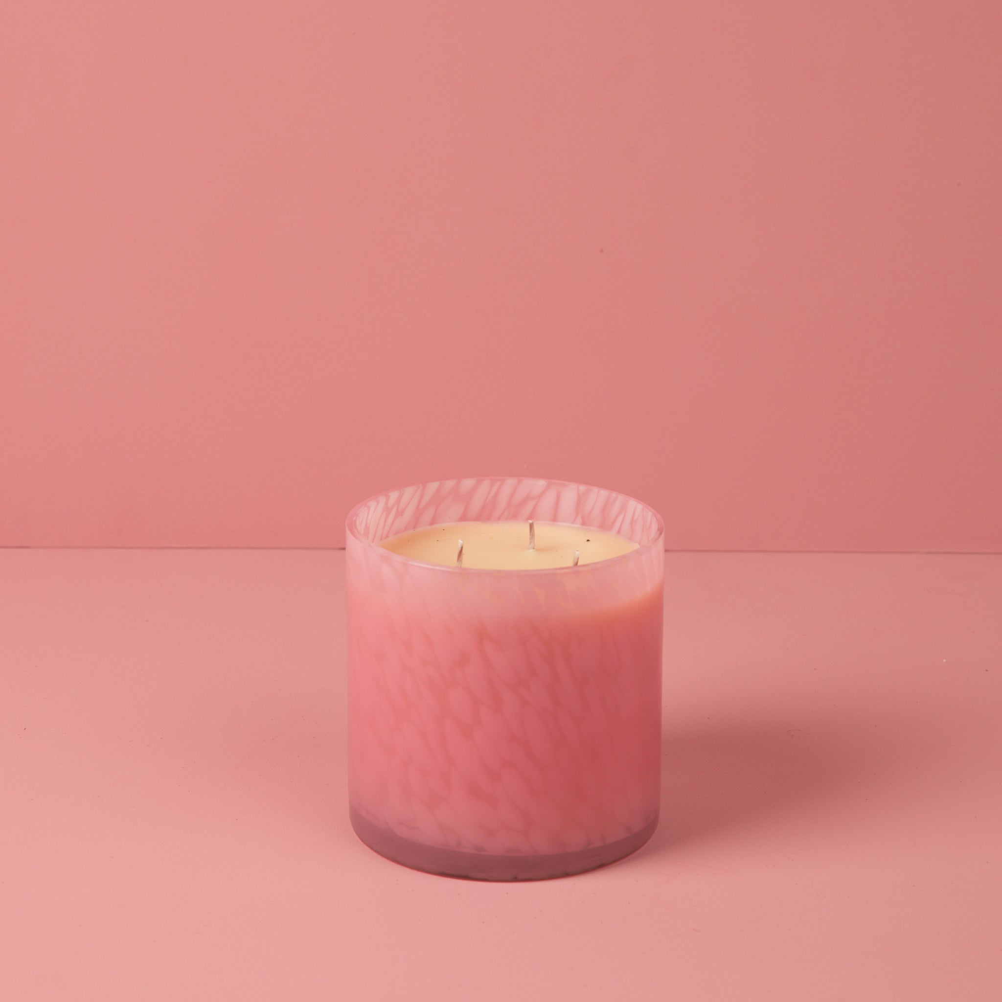 The Bridgewater Candle Sweet Grace Collection Candle #073, a pink marbled three-wick soy-blend candle, rests on a pink surface with a matching pink background.