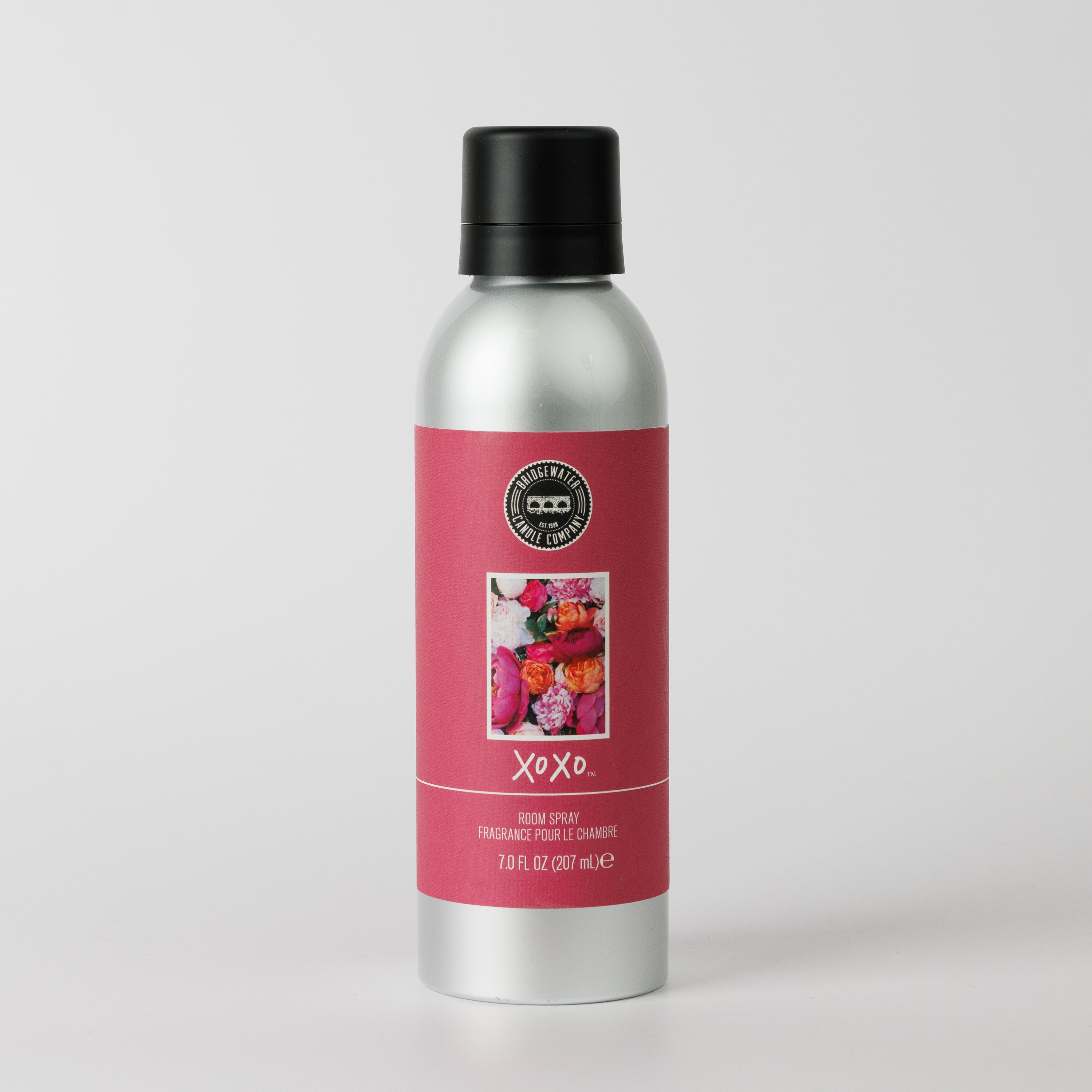A silver spray bottle with a black cap and a pink label featuring colorful flowers, Bridgewater Candle XOXO Non-Aerosol Room Spray, Peony & Damask Rose, 7 fl oz (207 ml)—an eco-friendly room spray with premium fragrance.