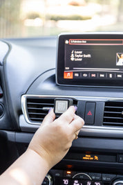 A hand attaches a Bridgewater Candle Auto Vent Clip-Sweet Grace to a car’s dashboard air vent.