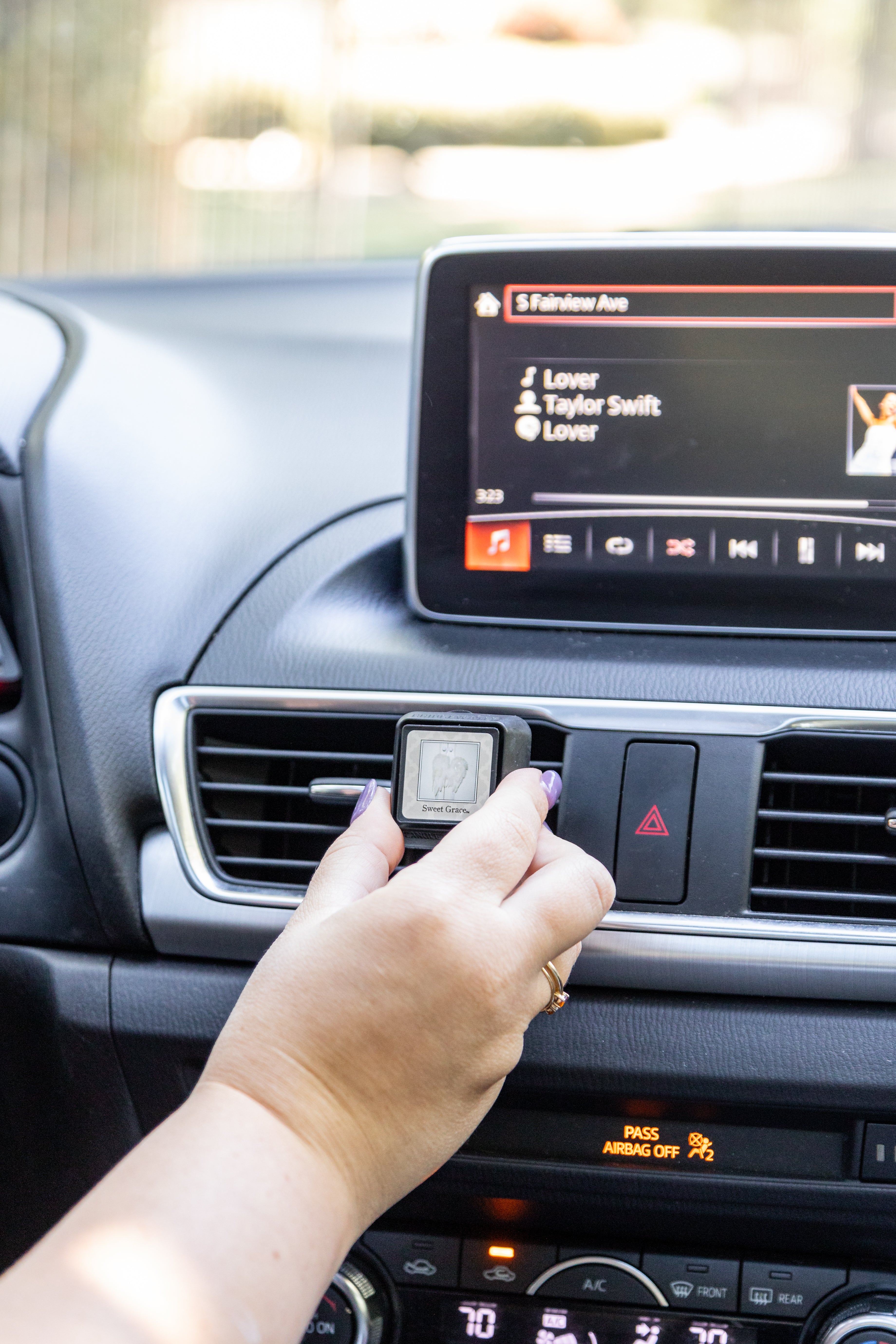 A hand attaches a Bridgewater Candle Auto Vent Clip-Sweet Grace to a car’s dashboard air vent.