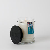 The Bridgewater Candle "I'll Be Home" 8oz Jar Candle features soy-blend wax in a clear glass jar with a black wooden lid, blue label, and small photo, shown against a plain white background.