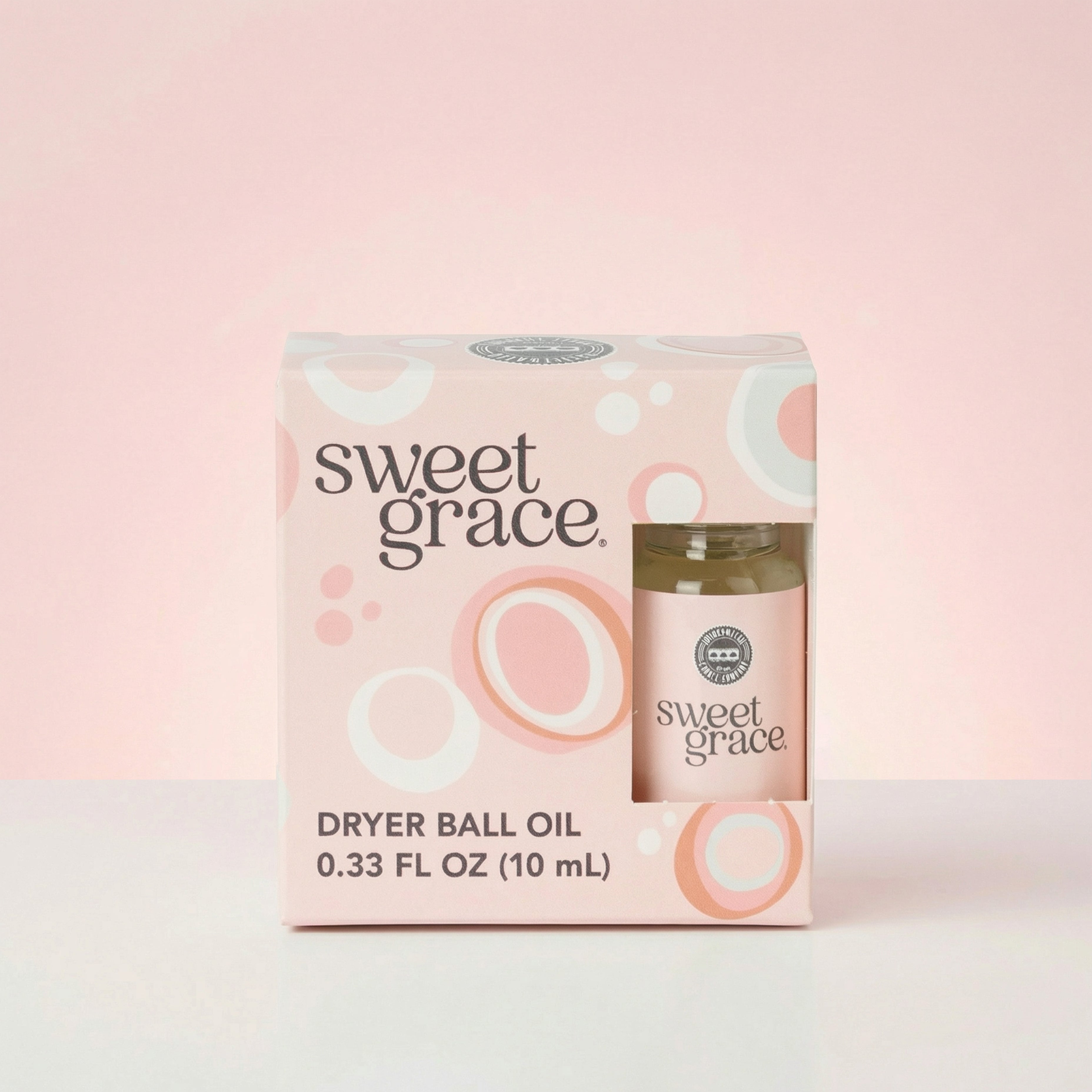 The Sweet Grace Dryer Ball Refill from Bridgewater Candle comes in a pink and white box with circular patterns and includes a 0.33 FL OZ (10 mL) laundry fragrance, ideal for use with wool dryer balls, set against a soft pink background.