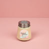 The Bridgewater Candle Sweet Grace Collection Candle #078, featuring cream-colored soy-blend wax in a petite glass jar with a metal lid, sits on a pink surface with a pastel label against a matching background.