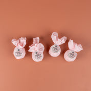 The Bath Bomb 4 Pack-Sweet Grace by Bridgewater Candle features four round bath bombs, wrapped in pink tissue with white labels, arranged side by side on a salmon-colored background.