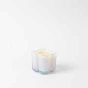 The Bridgewater Candle Sweet Grace Collection Candle #076 is a white flower-shaped soy-blend candle in a translucent glass holder with blue and purple tones, shown against a plain white background.