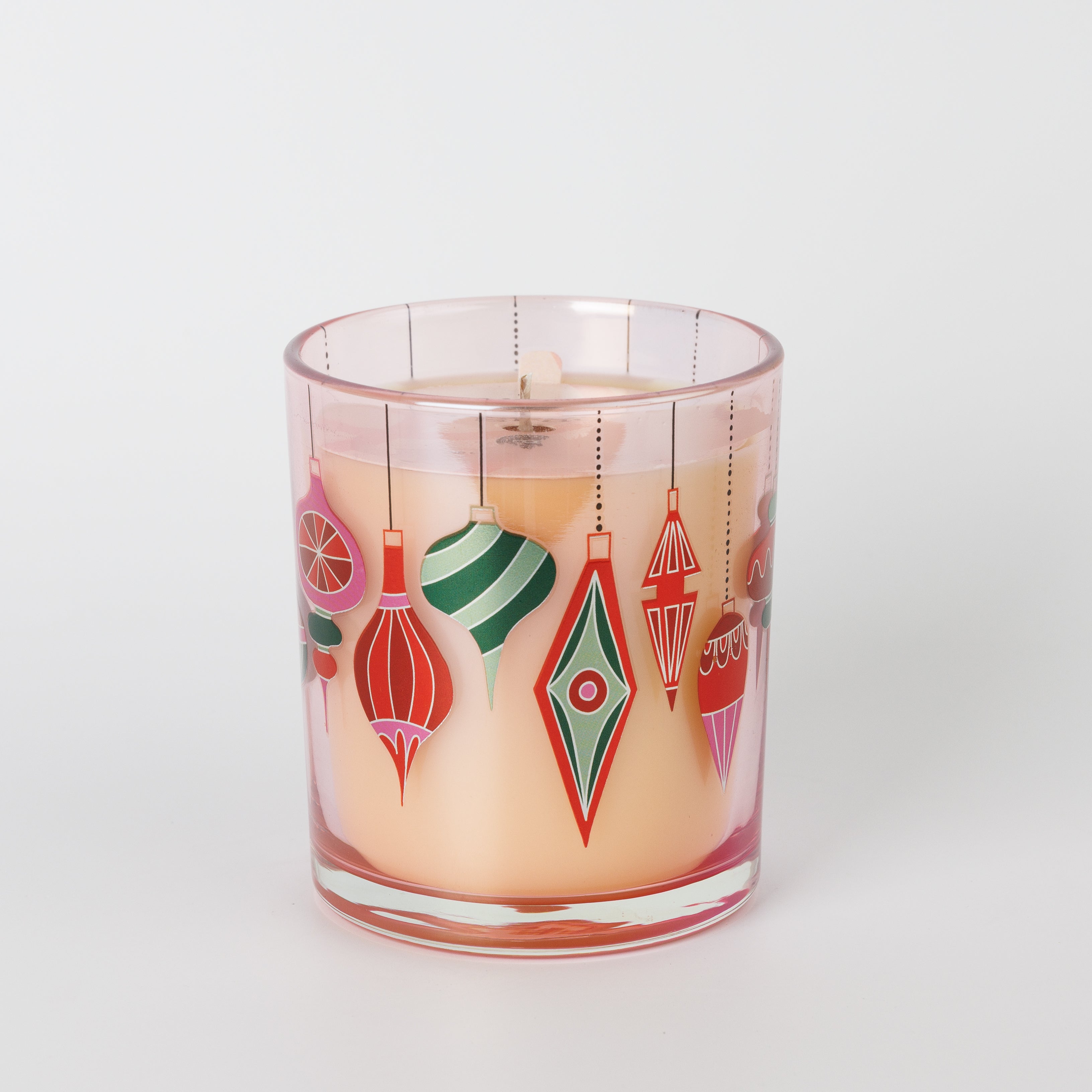 The Bridgewater Candle Sweet Grace Ornament Decal Candle features a glass holder filled with light peach, soy-blend wax and is adorned with colorful, retro-style holiday ornament illustrations in red, green, and pink on the outside.