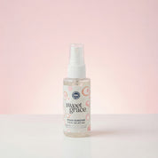 A small Bridgewater Candle Sweet Grace Stain Remover - Travel Size stands upright on a white surface with a soft pink gradient background. Its label displays pink and beige circular patterns.