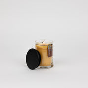 The Bridgewater Candle Autumn Gold Small Jar Candle, made with soy-blend wax and a warm fall scent, sits in a glass jar with its black textured lid beside it on a white background. A small product label accents the jar.