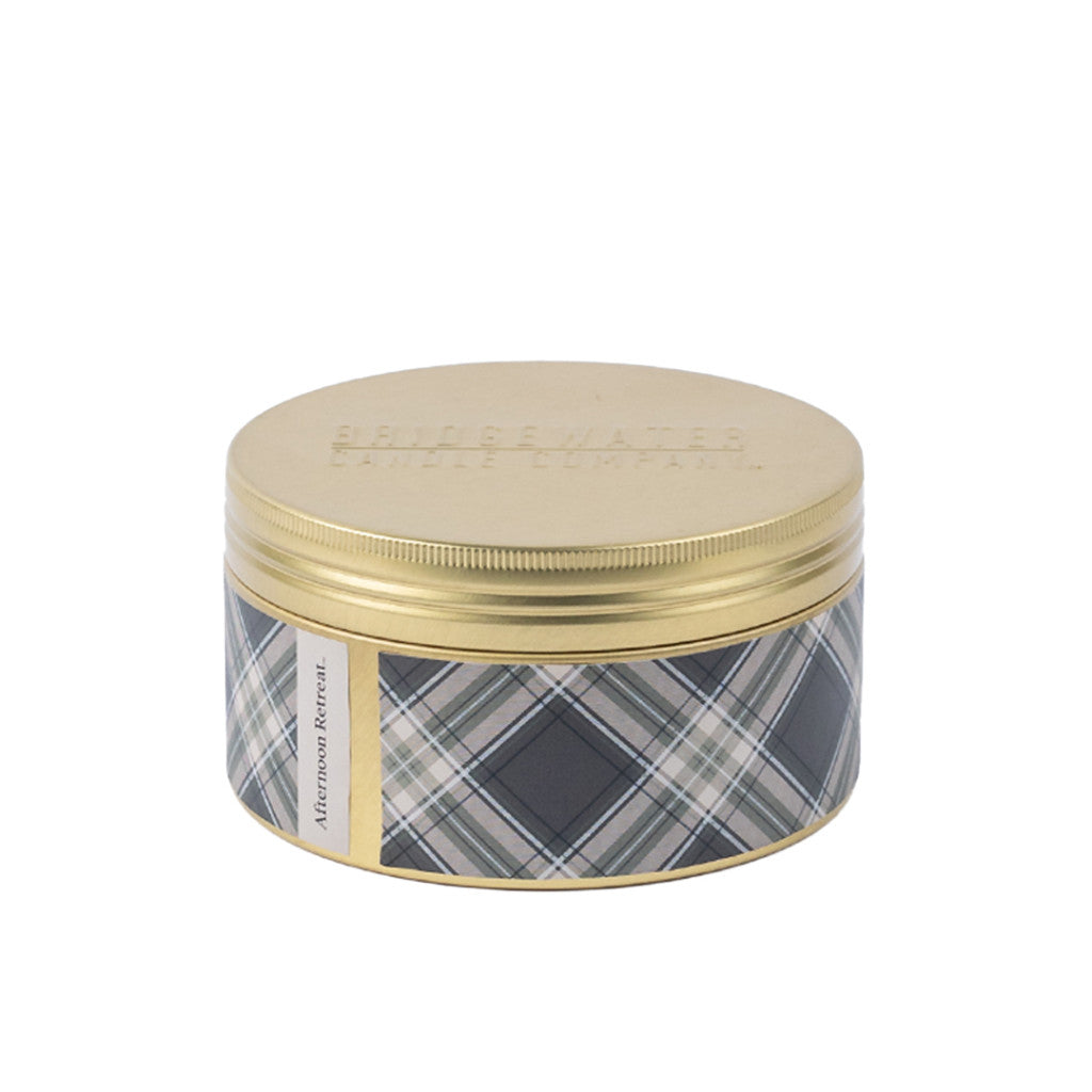 Bridgewater Candle Companys Afternoon Retreat 3-Wick Tin Candle comes in a round metal tin with a gold lid and blue, gray, and white plaid sides. The soy-blend wax ensures a clean burn, perfect for an inviting Afternoon Retreat atmosphere.