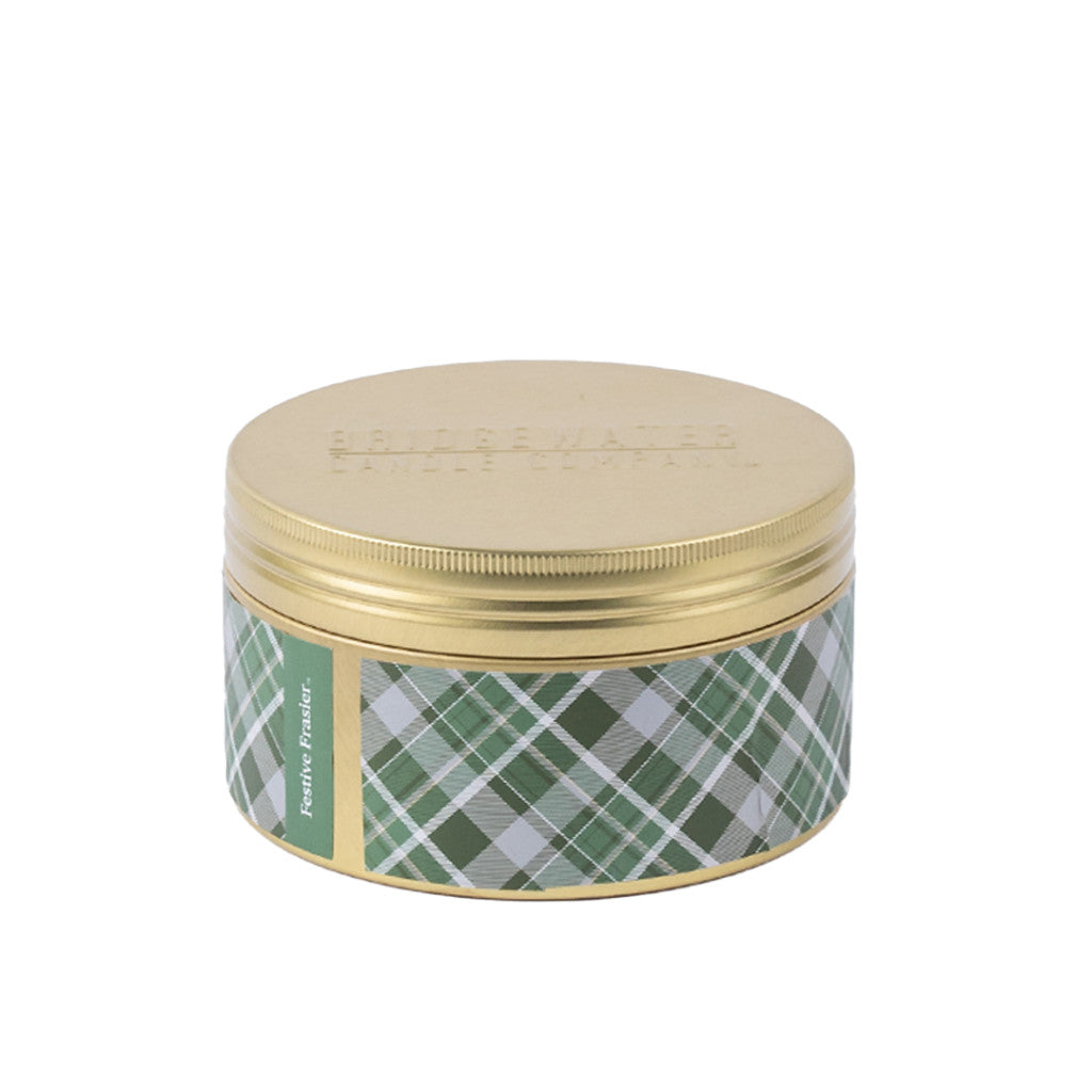 The Bridgewater Candle Company Festive Frasier Holiday 3-Wick Tin Candle features a round tin with a gold lid and green, white, and gray plaid sides. Made with soy-blend wax, it adds a cozy holiday touch.