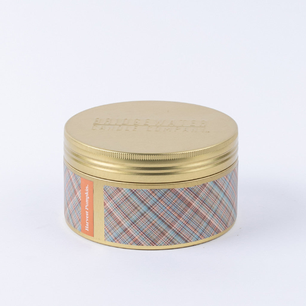Against a plain white background, the Bridgewater Candle Company Harvest Pumpkin 3-Wick Tin Candle is displayed in a gold tin container featuring a plaid patterned label with orange accents.