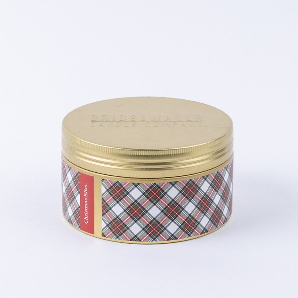 The Bridgewater Candle Company Christmas Bliss Holiday 3-Wick Tin Candle features a round tin with a gold embossed lid and plaid red, green, and white sides labeled "Christmas Bliss." Filled with festive soy-blend wax for holiday cheer.